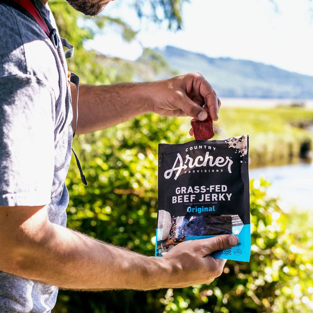 person eating a bag of Country Archer grass fed beef jerky on a hike