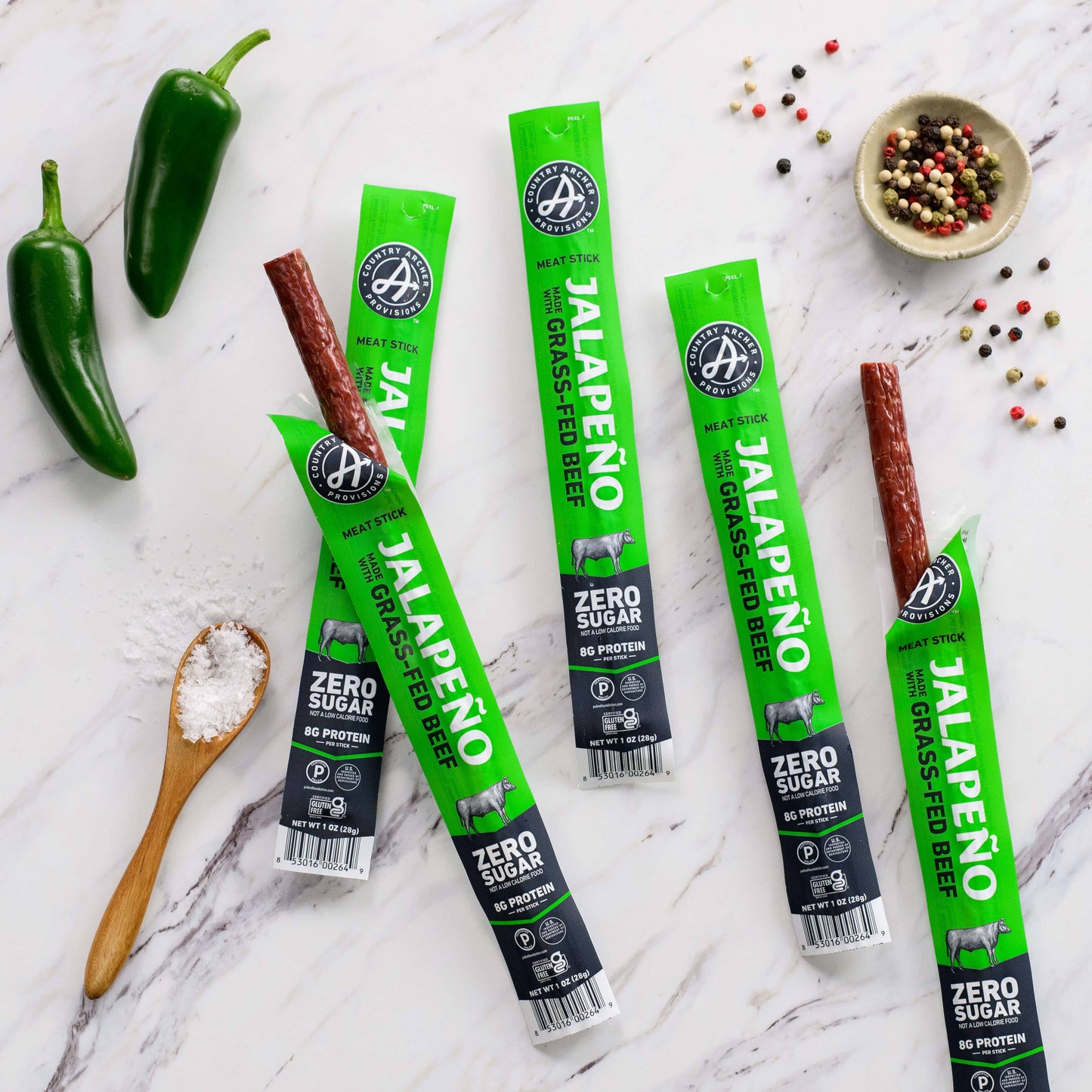 Country Archer Jalapeno grass-fed beef sticks on a marble countertop with peppers and spices.